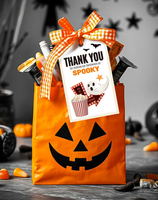 An orange Halloween-themed gift bag with a jack-o-lantern face, tied with an orange checkered ribbon. Attached to the bag is a Halloween_Spooky_Movie_Night_Tag_main featuring a cute ghost, popcorn, and 'Thank You for making our Halloween so spooky' text. The bag is filled with candy and Halloween treats, creating a festive atmosphere with pumpkins and bats in the background.